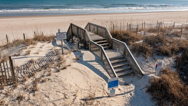 A wooden staircase leading to a beach with a warning sign about dunes and a fine for trespassing.