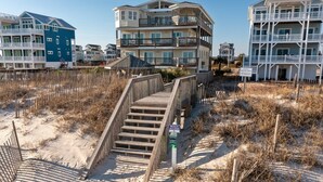A beach access boardwalk leading to a multi-story beachfront building with balconies.