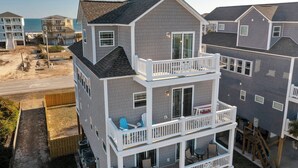 A two-story beachfront house with a balcony, a pool, and a view of the ocean.