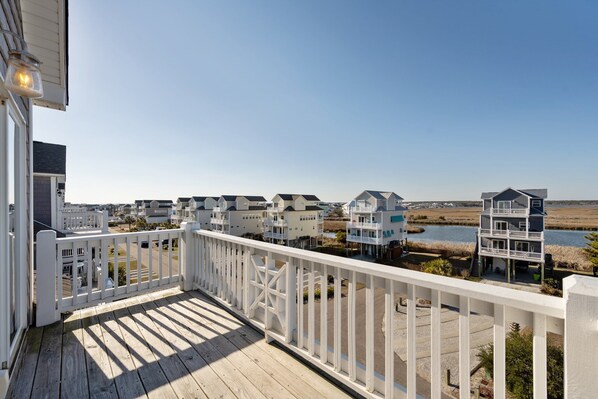 A wooden deck with a white railing overlooking a coastal area with multiple buildings and a body of water.