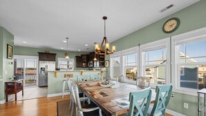A spacious kitchen with a large island, wooden dining table, and teal chairs.