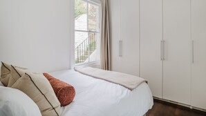 A bedroom with a bed, white curtains, and a view of a brick building outside. - Spacious Luxury Flat with Garden in Central London (London)