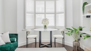 A corner room with a bay window, a round table with two chairs, a green sofa, and a potted plant. - Spacious Luxury Flat with Garden in Central London (London)
