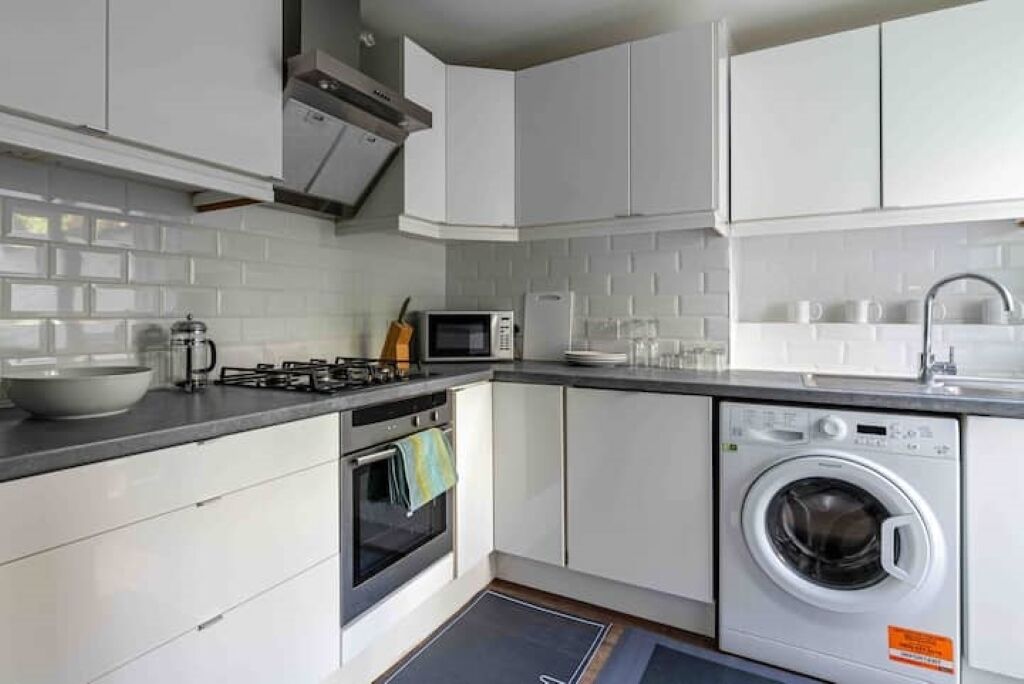 A modern kitchen with white cabinets, a stove, microwave, and a washing machine.