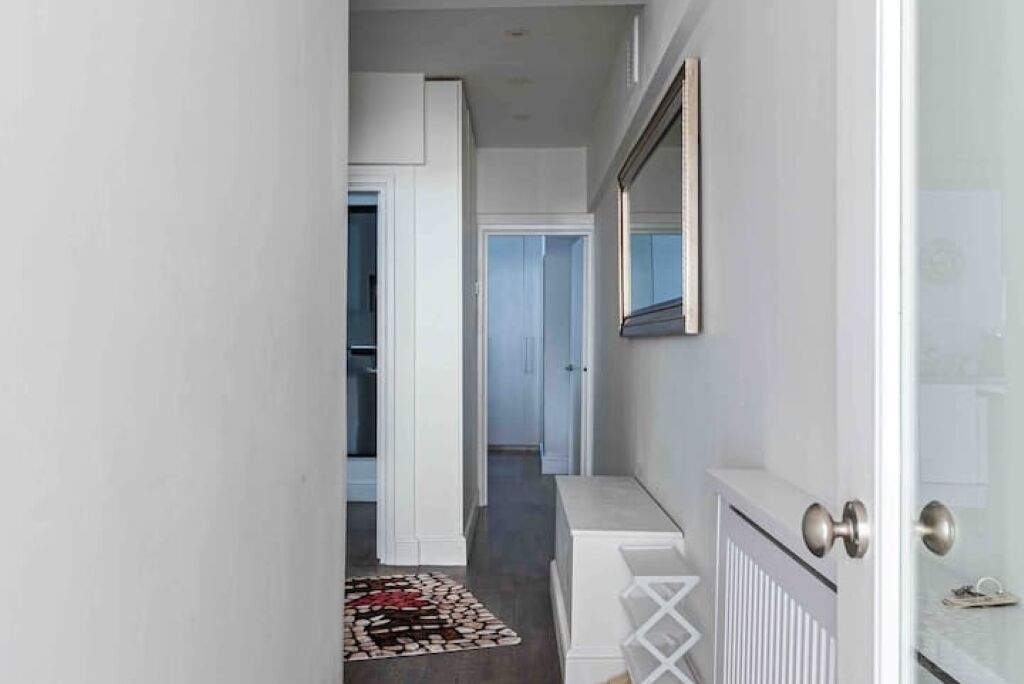 A narrow hallway with a white door, a radiator, and a small rug.
