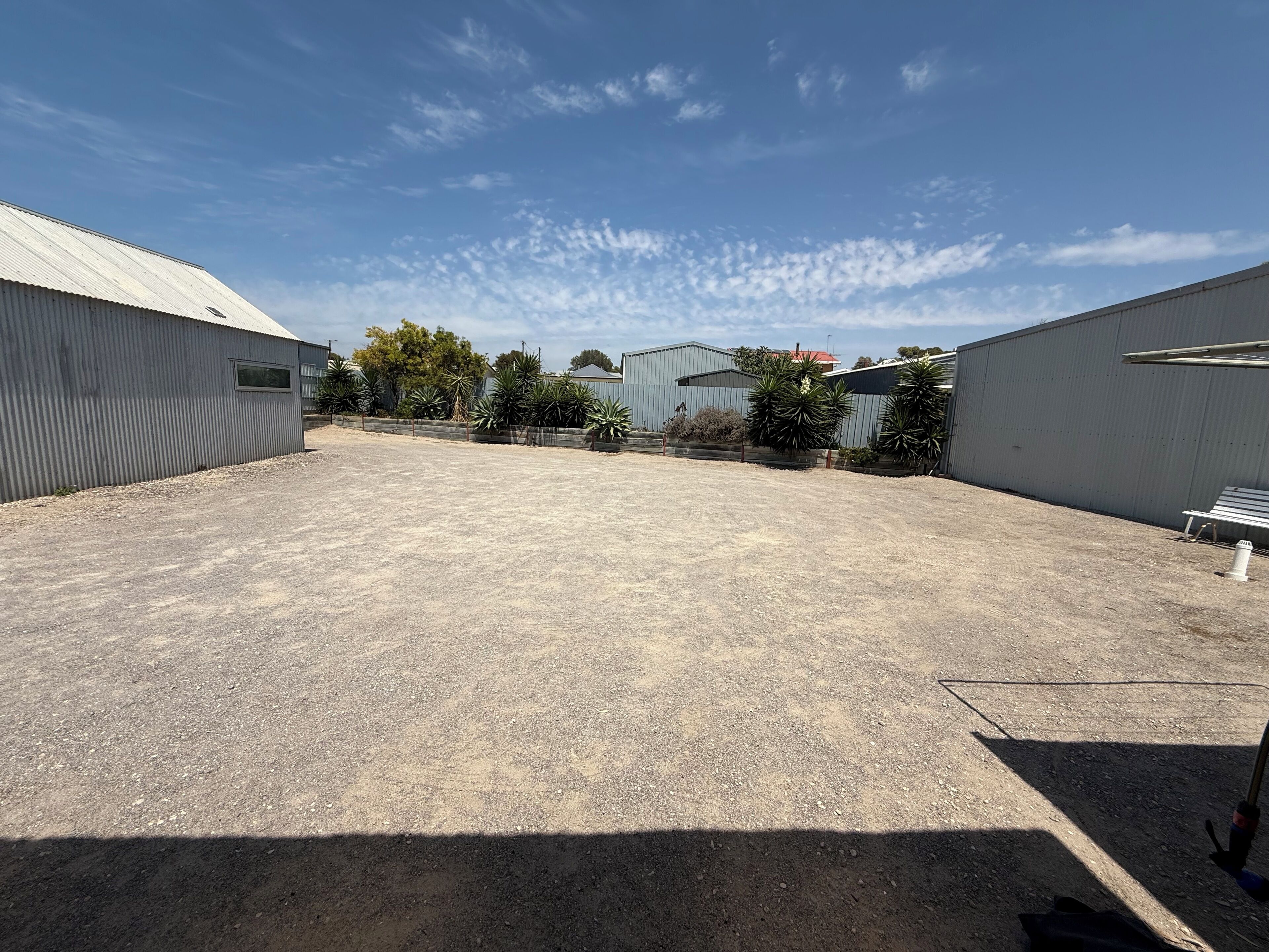 Un espace extérieur doté d’un sol en gravier, entouré de bâtiments industriels et agrémenté de quelques espaces verts.