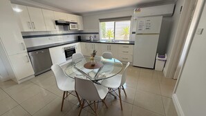 A modern kitchen with white cabinets, a glass dining table, and a built-in oven.