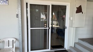 A sliding glass door leading to a porch with a white plastic chair and a brown mat.