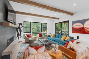 A modern living room with a fireplace, large windows, a blue sofa, and a coffee table.
