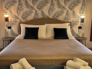 A hotel room with a large bed, two pillows, a quilted bedspread, and a wall with a leaf pattern. There are two bedside tables with lamps. - Il Bivio (Ostellato)