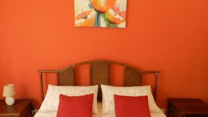 Una cama con dos almohadas rojas, un cabecero de madera y un cuadro en la pared.