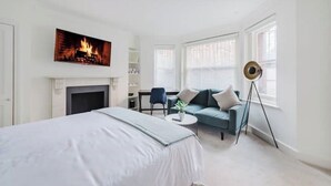 A modern bedroom with a bed, a blue sofa, a floor lamp, and a fireplace. - Luxury Flat in a Great Location / Harrods (London)
