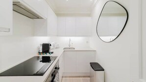 A compact kitchen with white cabinets, a black countertop, and a round mirror on the wall. - Luxury Flat in a Great Location / Harrods (London)