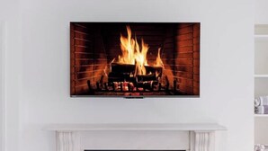 A flat-screen TV mounted above a fireplace with a visible fire. - Luxury Flat in a Great Location / Harrods (London)