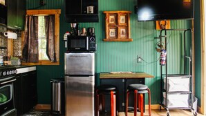 A compact kitchen with a refrigerator, microwave, and stove. There are two stools and a small table.