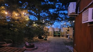 An outdoor patio area with a wooden bench, a fire pit, and string lights.