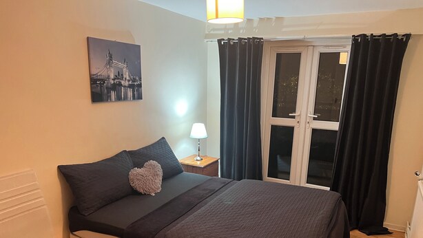 A bedroom with a bed, a chair, a nightstand, a lamp, a window with curtains, and a picture on the wall. - 1 double room in London with WiFi (London)