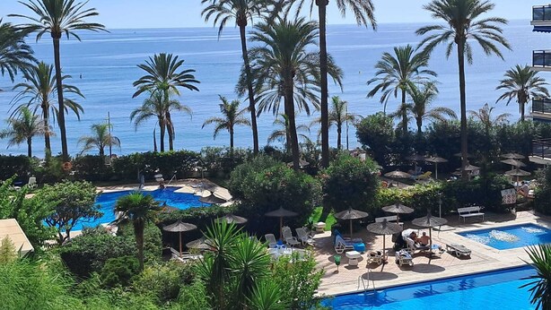 Resort com várias piscinas rodeadas por palmeiras e áreas de descanso com guarda-sóis.