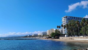 Paisagem costeira com praia, palmeiras e edifícios altos.