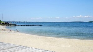A beach with a wooden pier extending into calm waters, a clear sky, and a distant landmass. - Sunset Island - 39 Fountain Drive West 3f 3 Bedroom Condo (Ocean City)