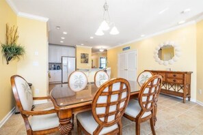 A dining area with a wooden table and chairs, a kitchen in the background, and a decorative mirror on the wall. - Sunset Island - 39 Fountain Drive West 3f 3 Bedroom Condo (Ocean City)