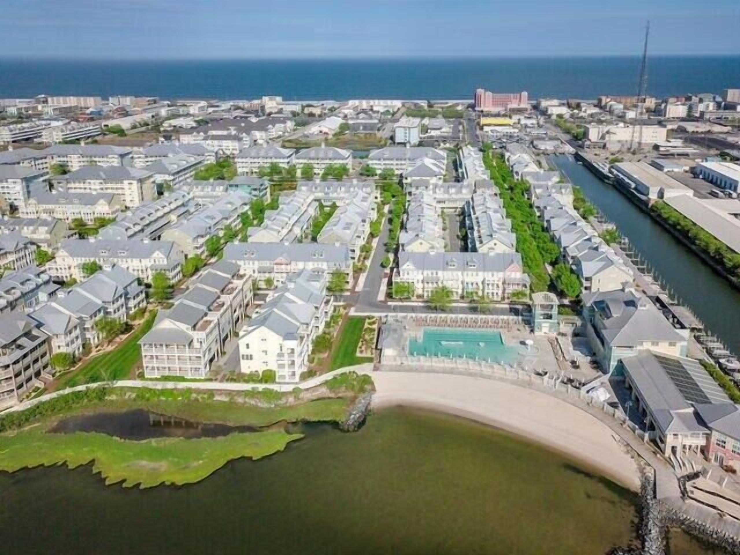 Eine Luftaufnahme einer Küstenwohngegend mit einer Marina, einem großen Gebäude mit Schwimmbad und einem Strand.