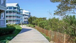 A wooden pathway leading to a multi-story building with balconies, surrounded by greenery and a wooden fence. - Sunset Island - 39 Fountain Drive West 3f 3 Bedroom Condo (Ocean City)