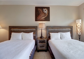 Ein Hotelzimmer mit zwei Betten, hölzernen Kopfteilen, einem Wandbild einer Eule und einem Nachttisch mit Lampe zwischen den Betten.