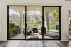 A modern interior with a sliding glass door leading to a patio with outdoor furniture and a view of a golf course.
