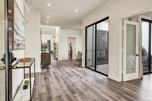 Un hall d’entrée spacieux avec un plancher en bois, une porte vitrée donnant sur un espace extérieur et un aménagement intérieur moderne.