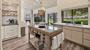 Een moderne keuken met een centraal eiland, inbouwapparatuur en een groot raam met uitzicht op een golfbaan.