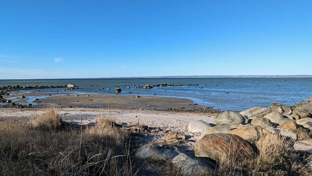Platja rocosa amb aigua tranquil·la i cel serè.