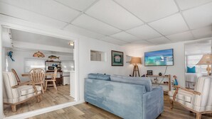 A living room with a blue sofa, wooden chairs, a dining table, and a kitchen area with a microwave and a small refrigerator. - JUDY'S PLACE ~ 2 Bedroom, 1 Bathroom in Venture Out Community! (Cudjoe Key)