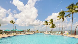 A clear blue pool surrounded by palm trees and beach chairs, with a view of the ocean and a clear sky. - JUDY'S PLACE ~ 2 Bedroom, 1 Bathroom in Venture Out Community! (Cudjoe Key)