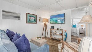 A living room with a sofa, a floor lamp, a television, and a decorative shelf. - JUDY'S PLACE ~ 2 Bedroom, 1 Bathroom in Venture Out Community! (Cudjoe Key)