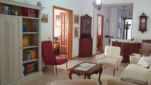 Ein Wohnzimmer mit Bücherregal, einem roten Sessel, einem weißen Sofa und einem Holzschrank.