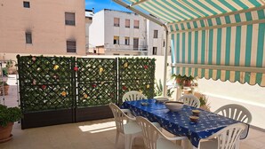 Eine Terrasse mit Esstisch, umgeben von weißen Stühlen und einem dekorativen Gitterzaun mit Blumen.
