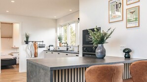 Eine moderne Küche mit Kochinsel, eine Essecke mit zwei braunen Ledersesseln und ein Wohnbereich mit Bett und Fernseher.
