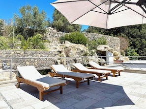 Outdoor lounge chairs with a stone wall and vegetation in the background.
