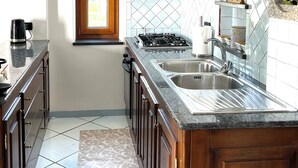 Une cuisine équipée d’une cuisinière à gaz, d’un évier à deux bacs, de meubles de rangement en bois et d’une fenêtre offrant une belle vue.