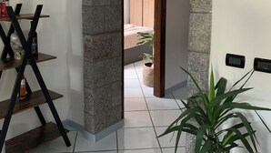Une pièce dotée d’une arche en pierre menant à un balcon, d’une chaise en bois, d’une plante en pot et d’une étagère où sont posées des bouteilles.