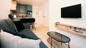 A modern living room with a sofa, a glass coffee table, and a TV mounted on the wall. - Le Majestic - T2 en centre ville (Annecy)
