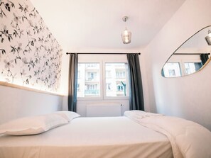 Une chambre à coucher avec un lit, une fenêtre avec des rideaux, un radiateur et un miroir fixé au mur.
