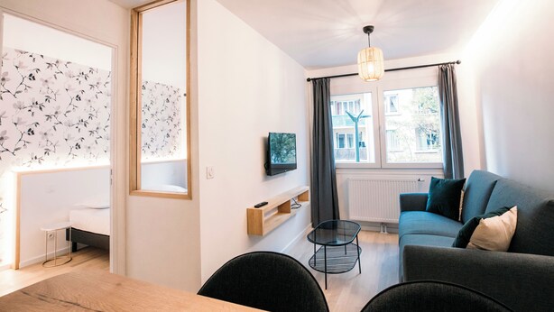 A modern living room with a sofa, a dining table, and a TV mounted on the wall. - Le Majestic - T2 en centre ville (Annecy)