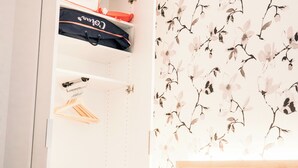 A closet with hanging clothes and a bag, a whiteboard, and a floral wall design. - Le Majestic - T2 en centre ville (Annecy)