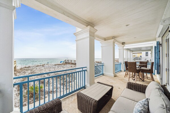 A covered outdoor area with wicker furniture, a view of the beach, and a dining table with chairs.