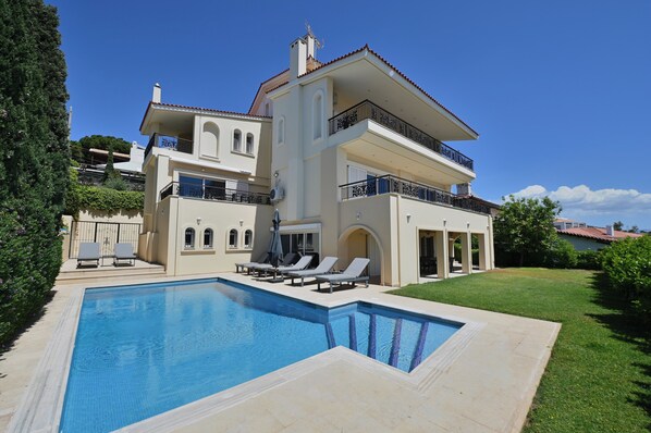 Ein großes, zweistöckiges Haus mit Swimmingpool, Sitzgelegenheiten im Freien und einem gepflegten Rasen.