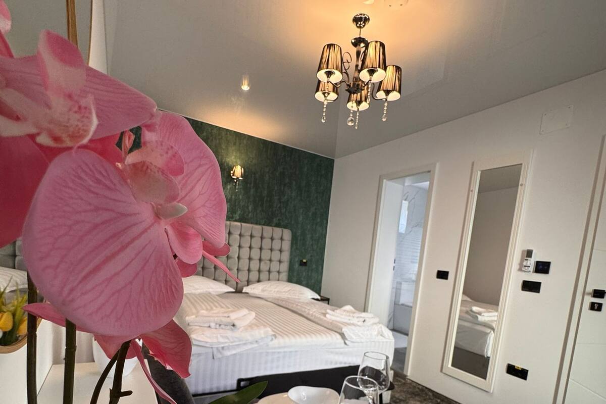 Una habitación de hotel moderna con una cama bien hecha, una zona de comedor con platos y cubiertos blancos, y una orquídea grande.