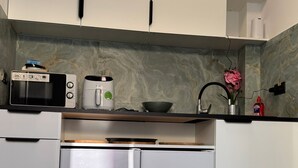 Una cucina moderna con mobili bianchi, forno a microonde integrato, macchina per caffè e frigorifero in acciaio inossidabile.