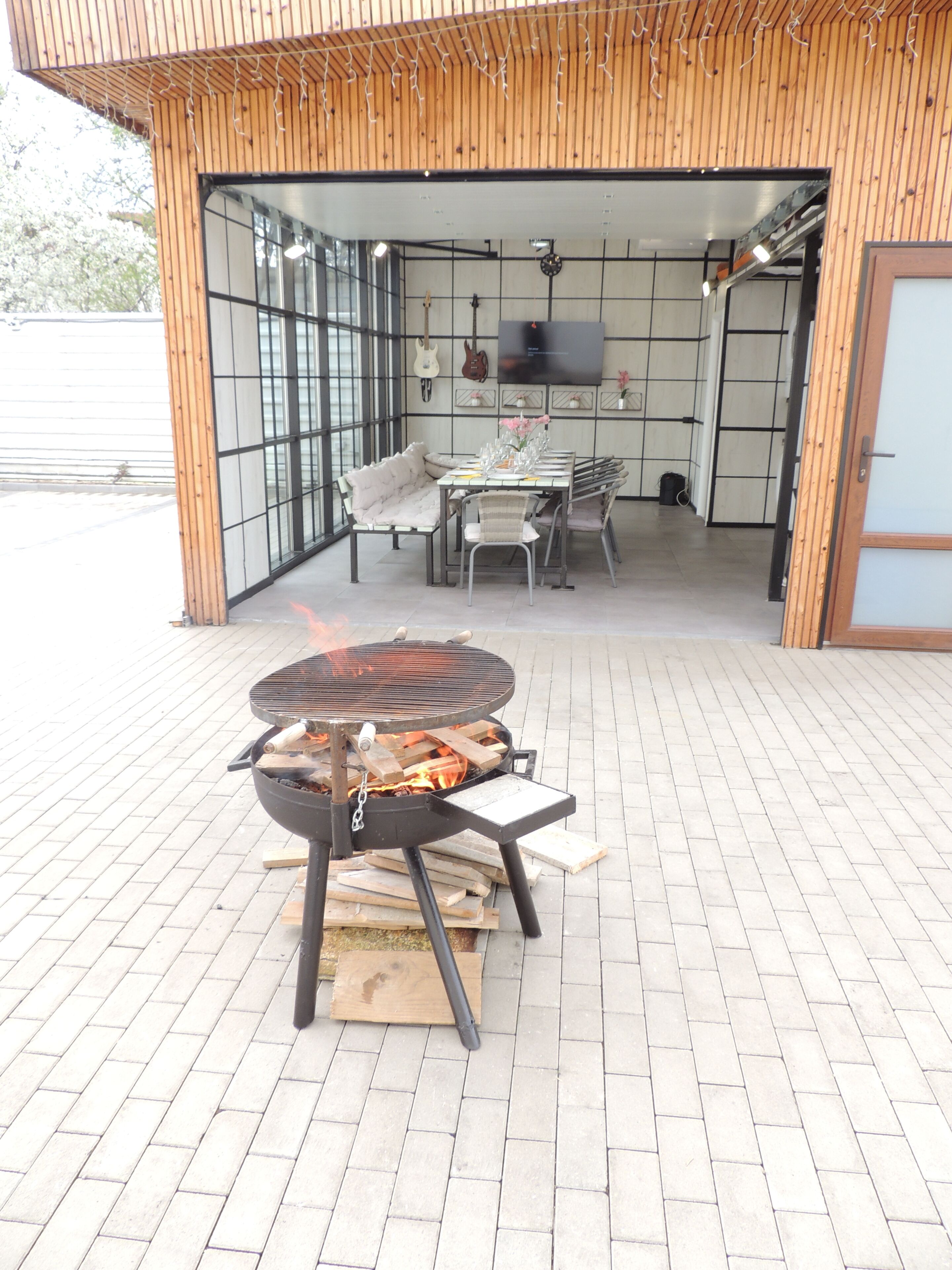 An outdoor patio with a grill, a dining table with chairs, and a television mounted on the wall.